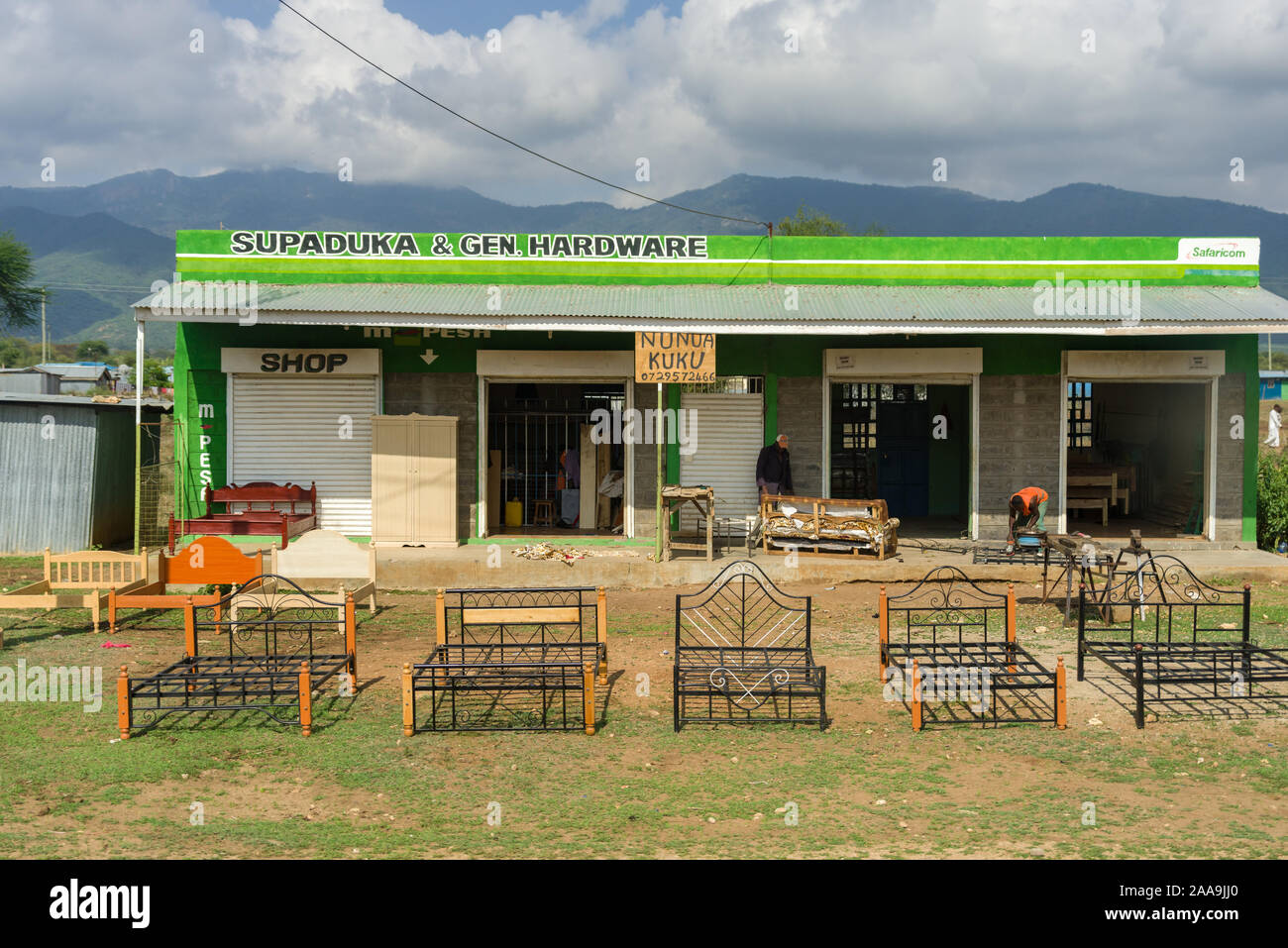 A small shop with bed frames on display outside on grass with workers