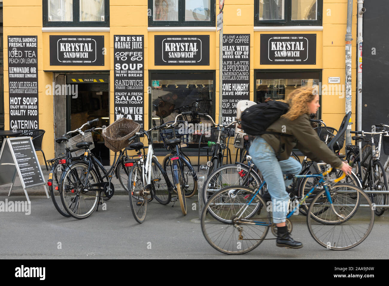 Copenhagen Latin Quarter, view of a young Danish woman cycling past a popular sandwich shop in Krystalgade in the old town Latin Quarter of Copenhagen. Stock Photo