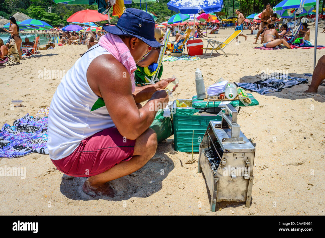 A male Brazilian beach vendor preparing Grilled Brazilian Cheese Skewers (Espetinhos de Queijo de Coalho) at Grumari Beach, Rio de Janeiro. Stock Photo