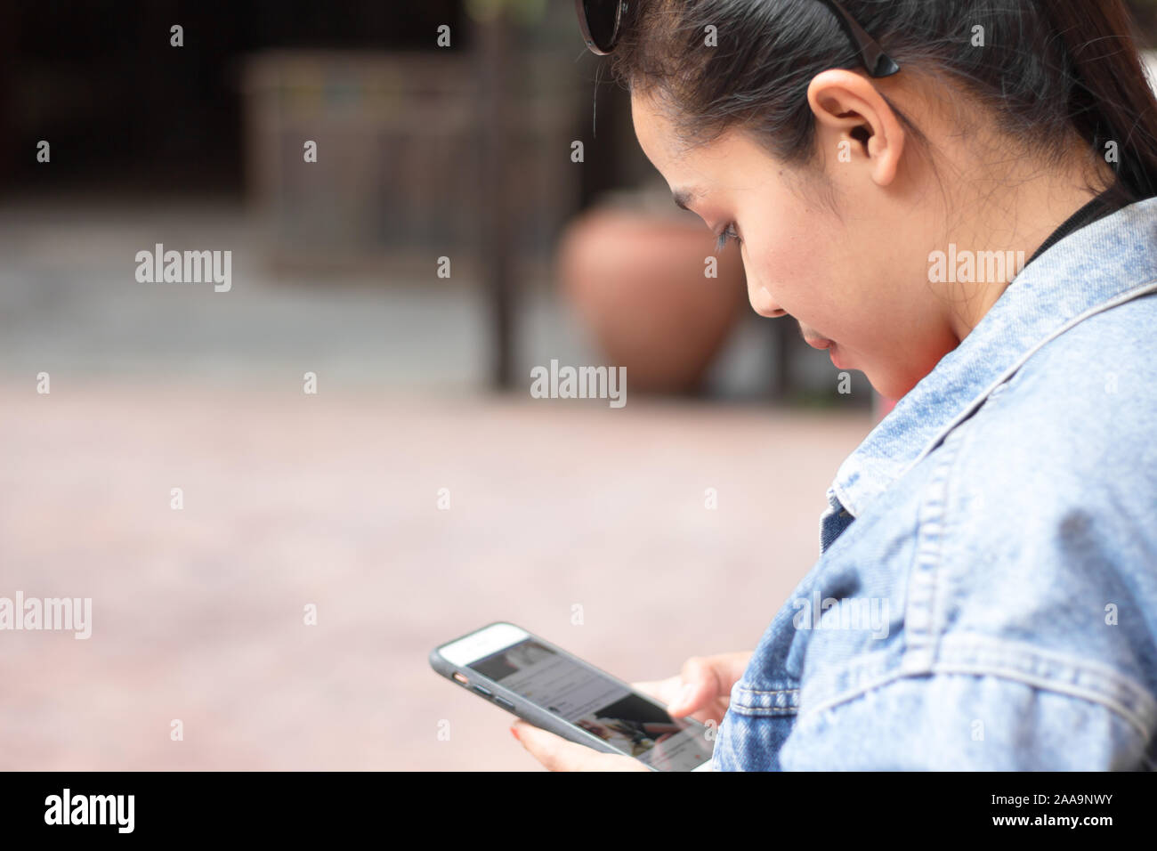 Behine teenage girl wearing a jacket, jeans and orange shirt and playing mobile phones. Stock Photo