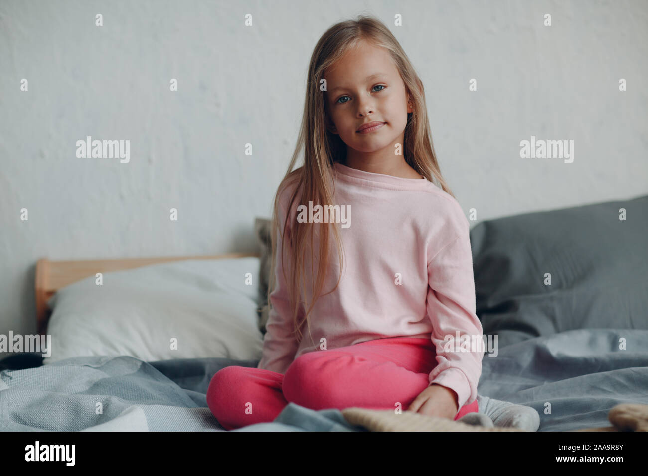 Positive smiling little girl portrait sitting on bed in bedroom Stock ...