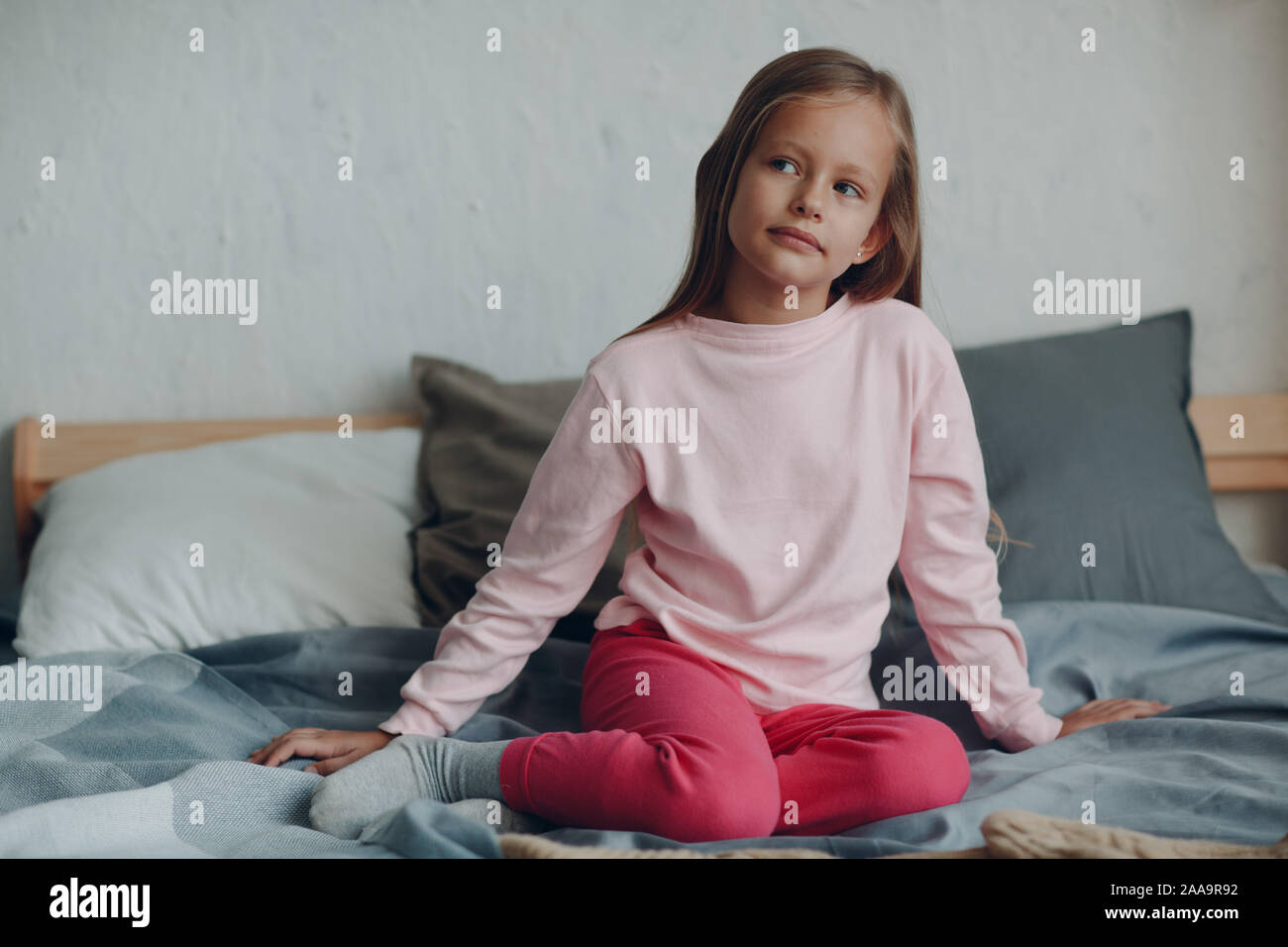 Positive smiling little girl portrait sitting on bed in bedroom Stock ...