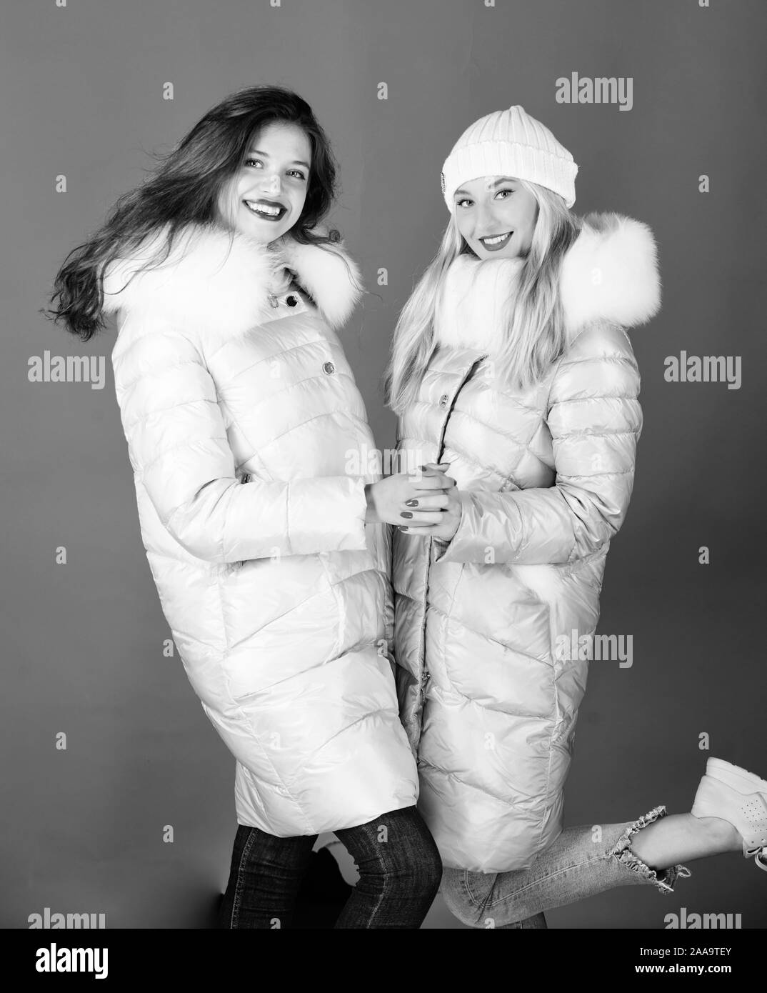 Women wear down jacket with furry hood. Girls smiling makeup faces wear  winter jackets blue background. Fashion friends. Winter season. Soft fur.  For those wishing stay modern. Winter clothes Stock Photo 
