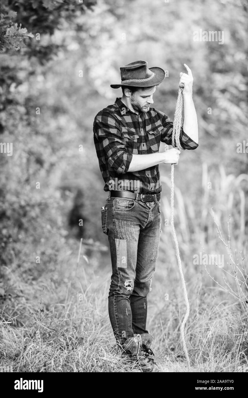 Cowboy at countryside. Man wearing hat hold rope. Ranch occupations. Lasso tool. American cowboy. Lasso tied wrapped. Western life. Man cowboy nature background. Ranch owner. attle breeding concept. Stock Photo