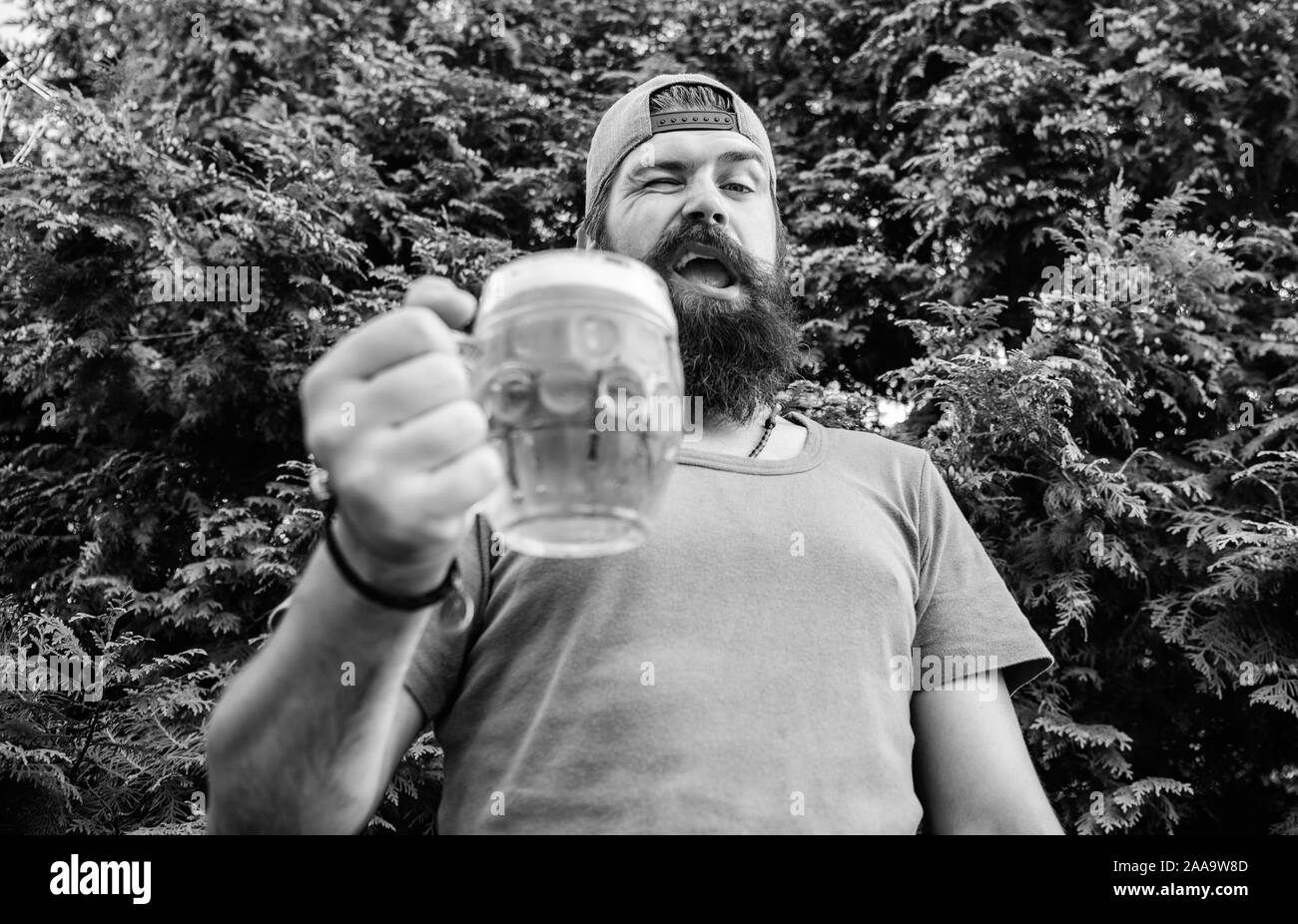 In playful mood. Brutal hipster with winking face having craft beer. Man drinker holding beer mug. Bearded man enjoy drinking beer on nature. Fun loving beer. Stock Photo