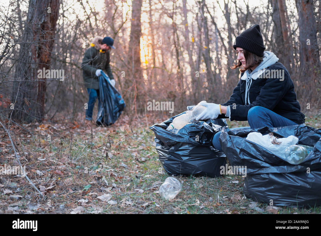 People clean up the forest of plastic trash. Environmental awareness concept: man and woman picking up plastic garbage from the woods while walking or Stock Photo