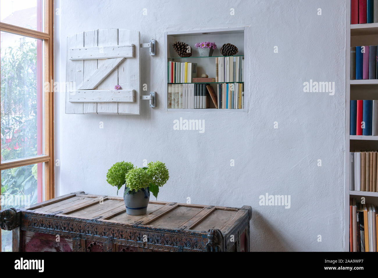 Entrance in a country house with flowers on a highboy and decorated bookshelves Stock Photo