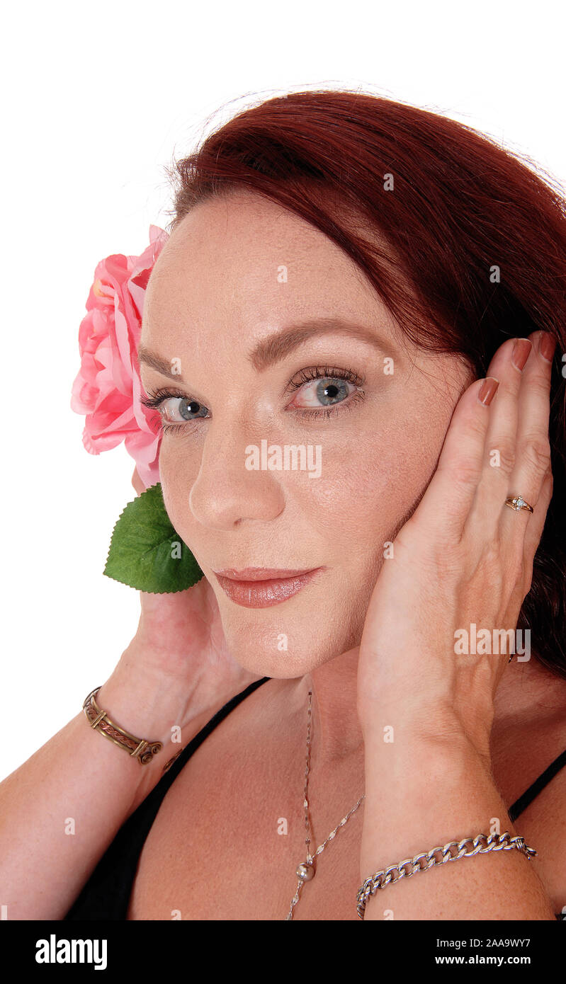 A close up picture of a pretty woman with long red hair holding one pink rose on her face, looking serious, isolated for white background Stock Photo