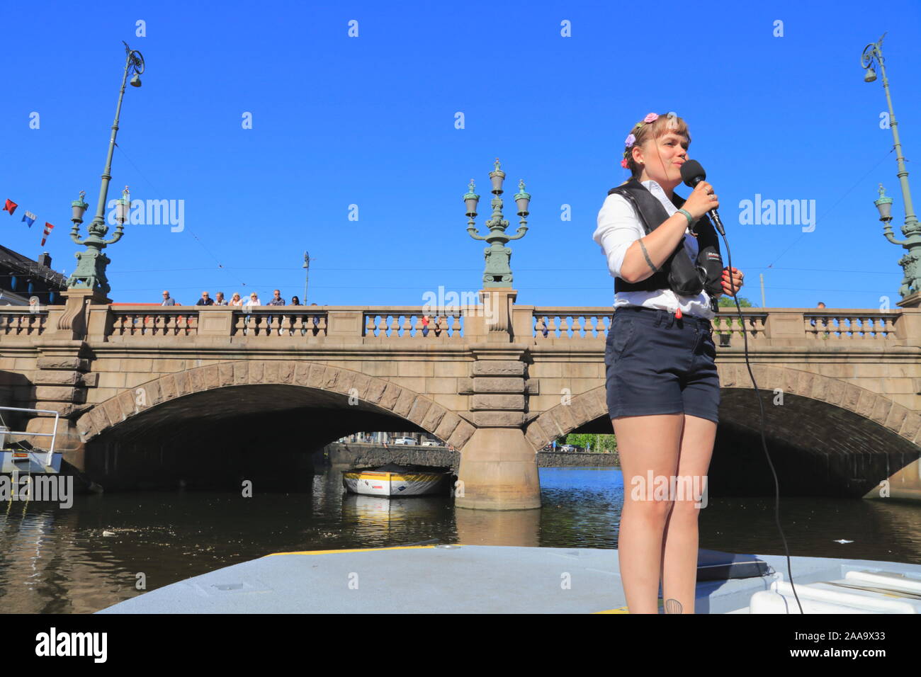 A tour guide provides information to tourists on the sightseeing boat Paddan in Gothenburg city, Sweden, while people look on from a bridge. Stock Photo