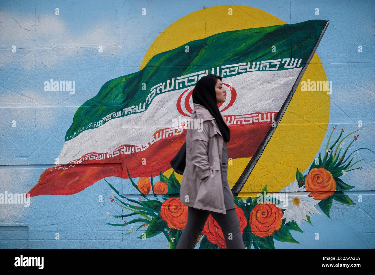 Tehran, Iran. 20th Nov, 2019. An Iranian woman walks next to a wall painting of the Iranian national flag in Tehran, Iran. Iran on 15 November increased fuel prices by at least 50 percent prompting protests in different cities. President Hassan Rouhani said the country's people had defeated an ''enemy conspiracy'' behind a wave of violent street protests. Demonstrations erupted in sanctions-hit Iran last week after an announcement the price of petrol would be raised by as much as 200 percent, with motorists blocking major roads in Tehran before the unrest spread rapidly to at least 40 urban Stock Photo