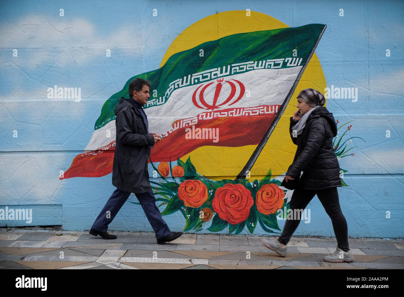 Tehran, Iran. 20th Nov, 2019. Iranians walk next to a wall painting of the Iranian national flag in Tehran, Iran. Iran on 15 November increased fuel prices by at least 50 percent prompting protests in different cities. President Hassan Rouhani said the country's people had defeated an ''enemy conspiracy'' behind a wave of violent street protests. Demonstrations erupted in sanctions-hit Iran last week after an announcement the price of petrol would be raised by as much as 200 percent, with motorists blocking major roads in Tehran before the unrest spread rapidly to at least 40 urban centers, Stock Photo