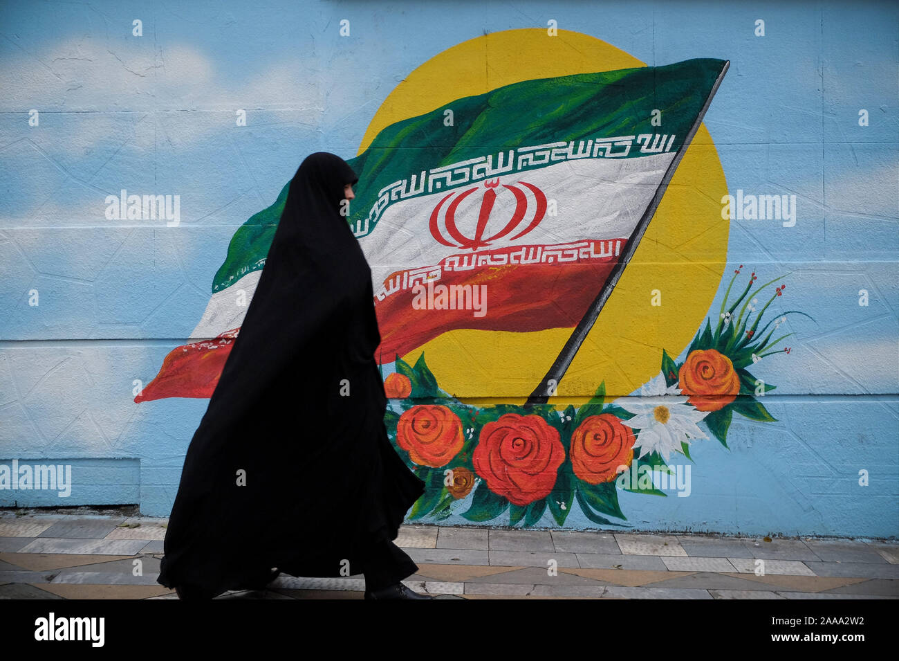 Tehran, Iran. 20th Nov, 2019. An Iranian veiled woman walks next to a wall painting of the Iranian national flag in Tehran, Iran. Iran on 15 November increased fuel prices by at least 50 percent prompting protests in different cities. President Hassan Rouhani said the country's people had defeated an ''enemy conspiracy'' behind a wave of violent street protests. Demonstrations erupted in sanctions-hit Iran last week after an announcement the price of petrol would be raised by as much as 200 percent, with motorists blocking major roads in Tehran before the unrest spread rapidly to at least 4 Stock Photo