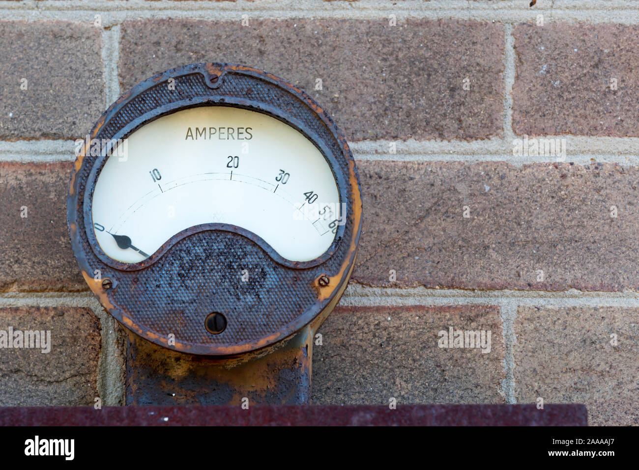 A rusting antique amp meter showing Amperes using a needle mounted outside on a brick wall Stock Photo