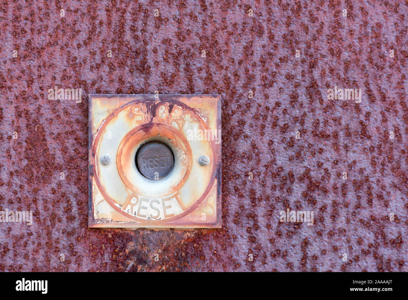 An old stop and reset button mounted on a rusted metal plate Stock Photo