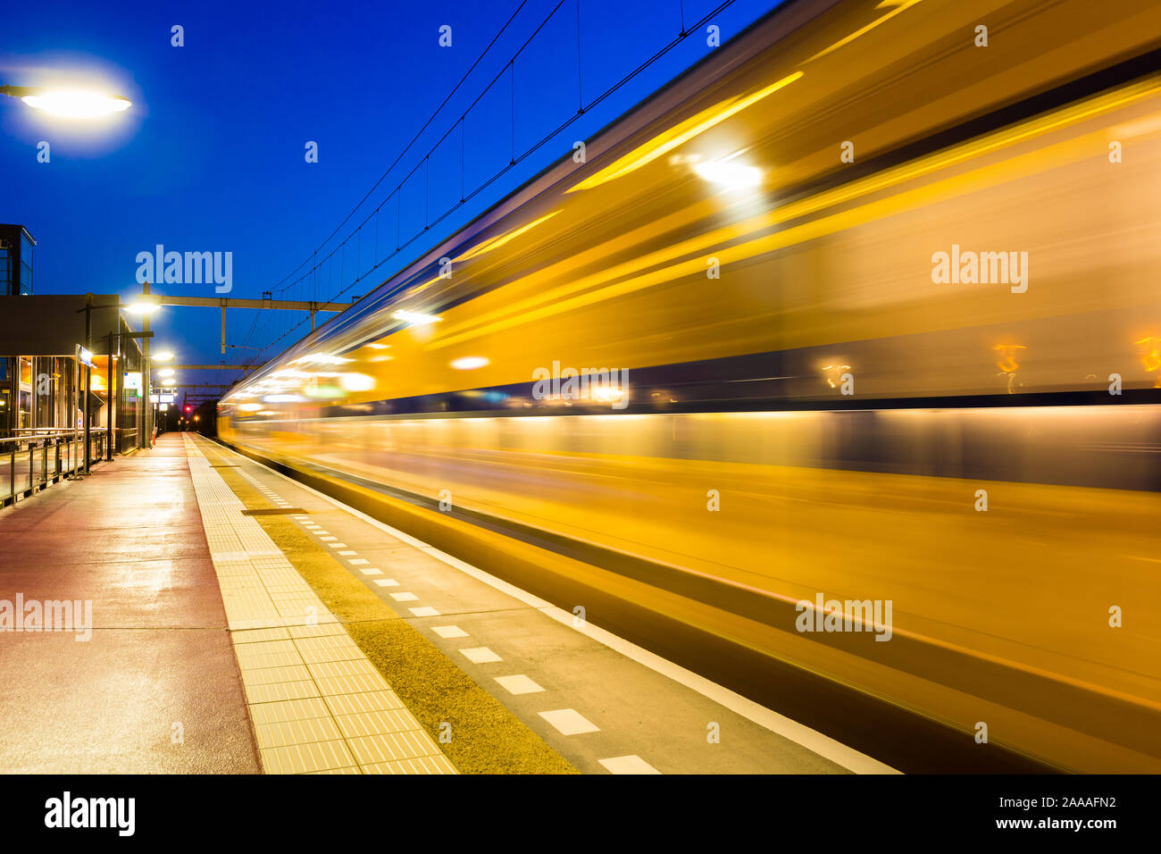 Blurred moving dutch train leaving the Amersfoort Vathorst station with an empty platform. Stock Photo