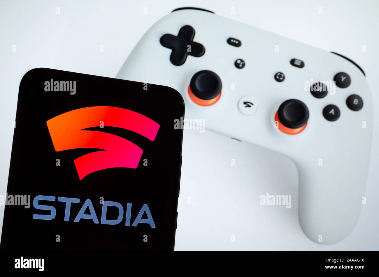 Stadia logo on a smartphone screen and white Google Stadia controller seen on the blurred background. Stock Photo