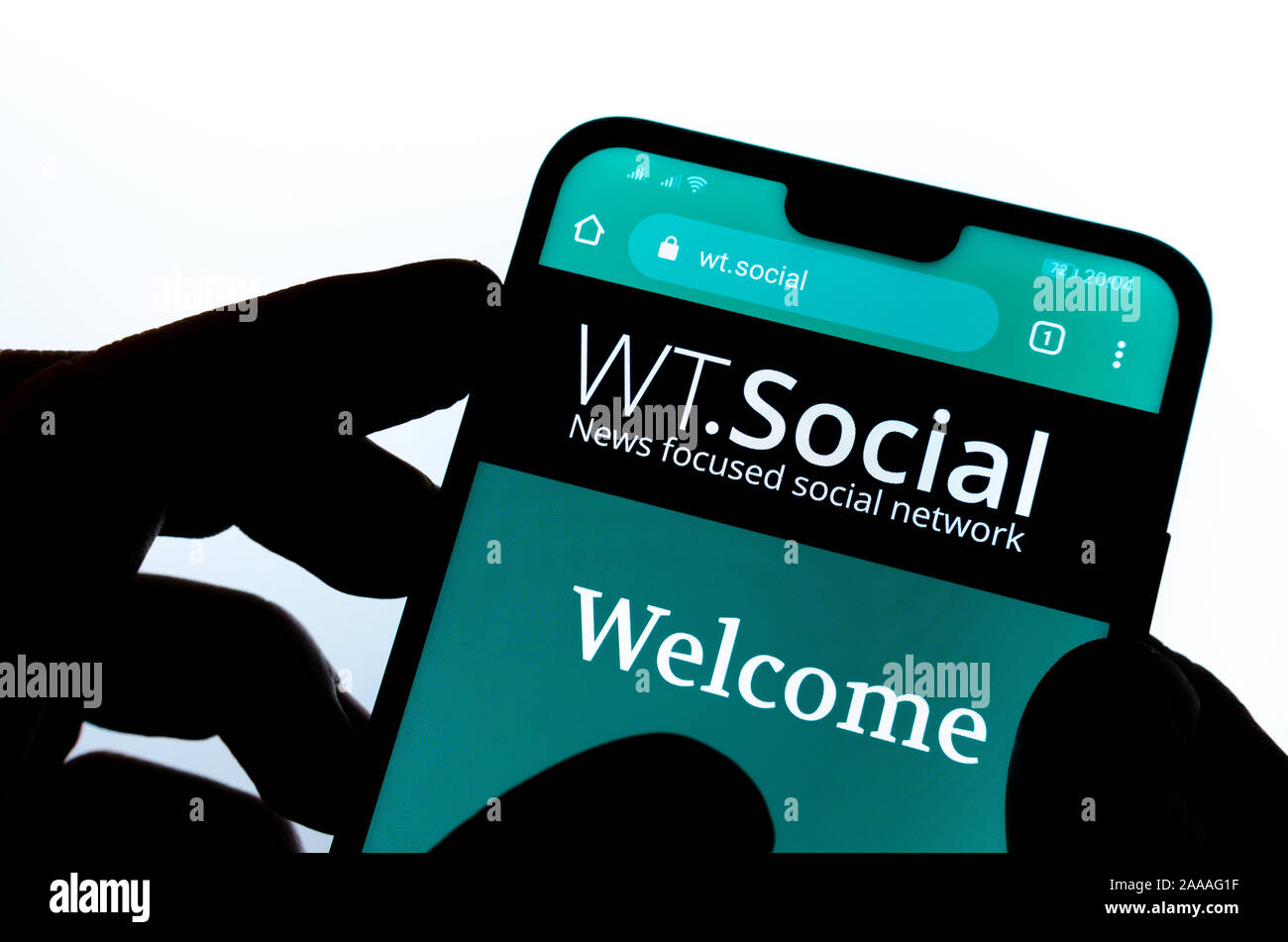 WT.Social website on the smartphone hold by a silhouette of a hand. WT:Social is news focused social network from Wikipedia founder. Stock Photo