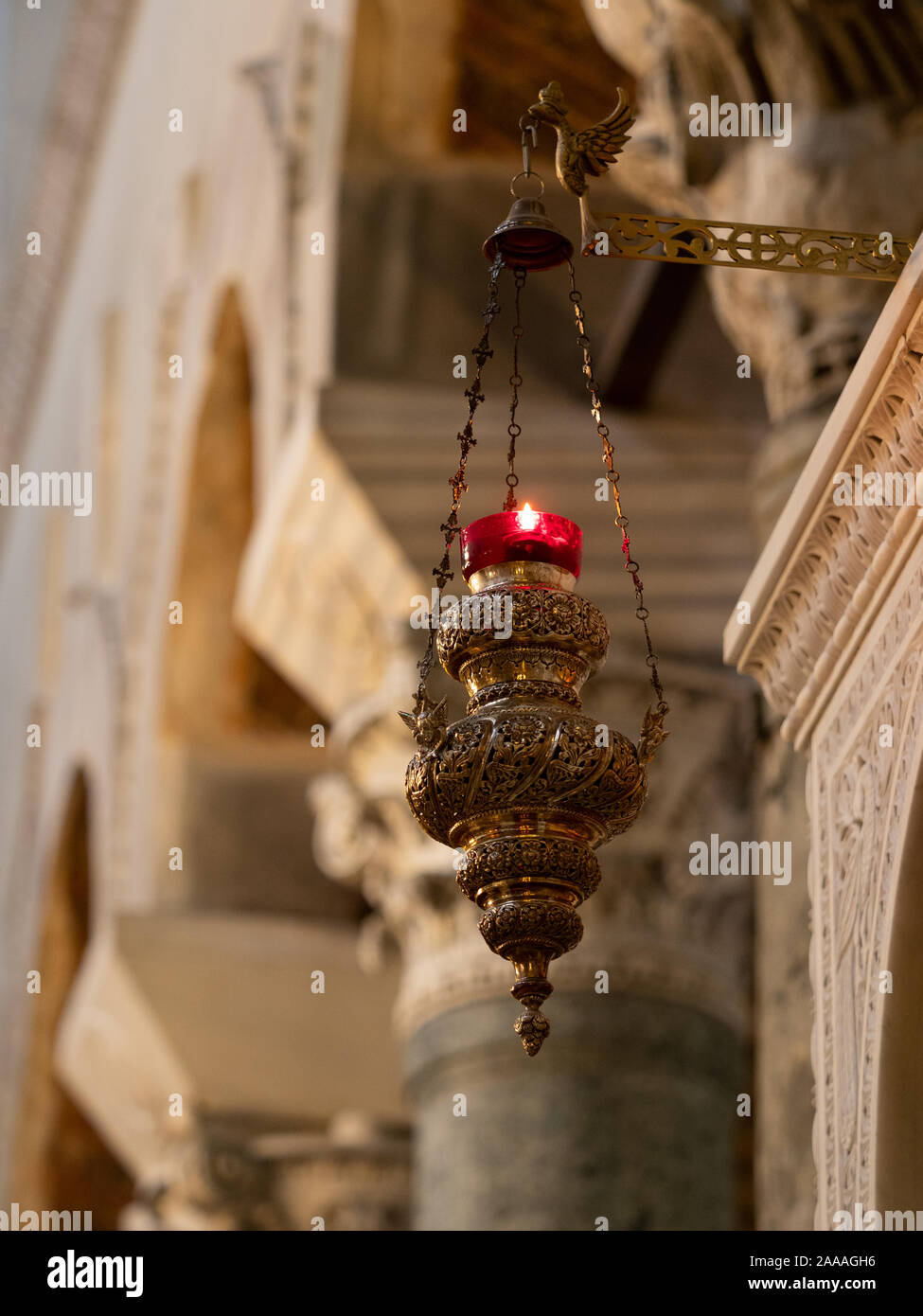 Close up of a hanging brass and red glass candle holder with lit candle hanging in St. Dimitrios Greek Orthodox Church in Thessaloniki, Greece. Stock Photo