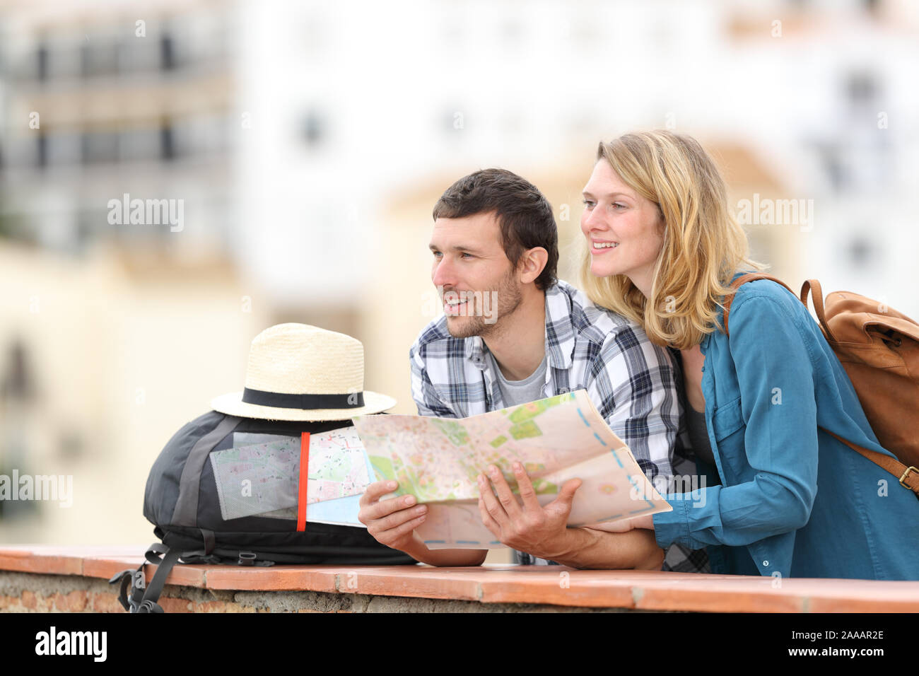 Happy couple of tourists sightseeing holding paper map standing outdoors in a balcony in a rural town Stock Photo