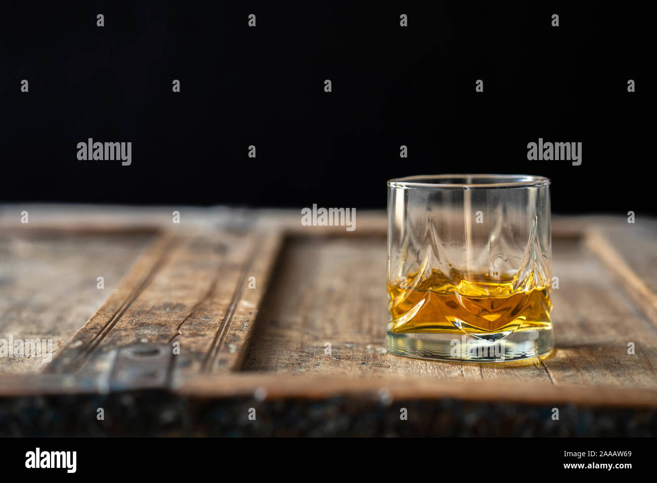 Low angle of a whisky glass with golden shimmering scotch on an old shabby wooden table Stock Photo