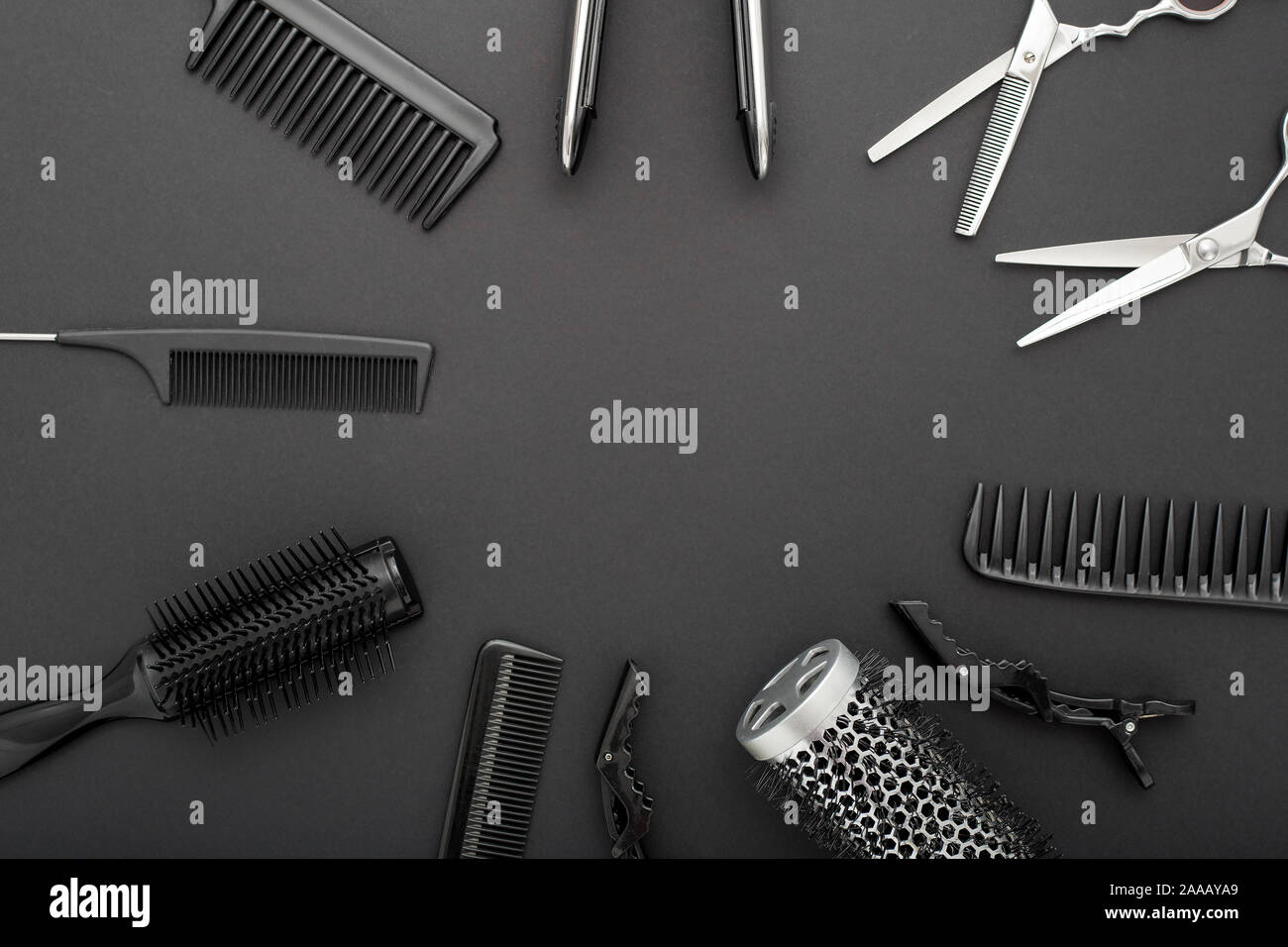 Flat lay composition with Hairdresser tools: scissors, combs, hair iron on black background with copy space for text in center. Frame. Hairdresser Stock Photo