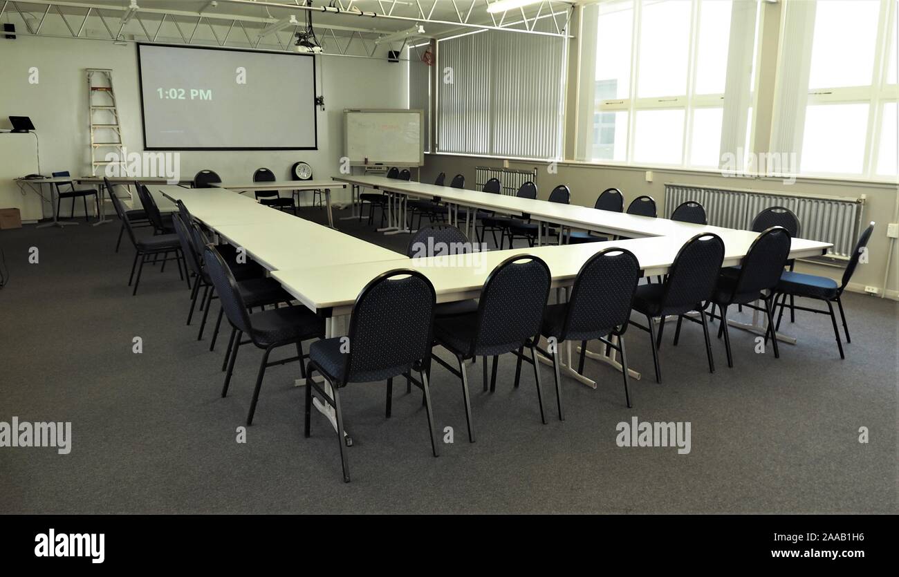 Large and empty meeting room in a typically bland layout. The time on the clock (1:02pm) suggests lunch time and everybody out. Stock Photo
