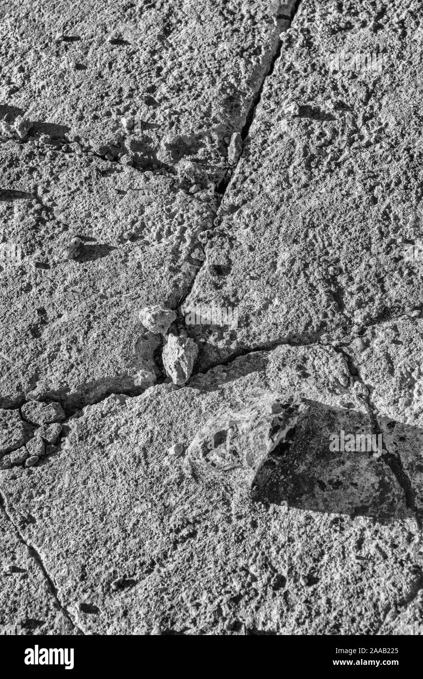 Black white of cracked rough cement surface with sun shadows on crevices. Metaphor cracks appearing, broken infrastructure, Colour version is 2AAB12W. Stock Photo