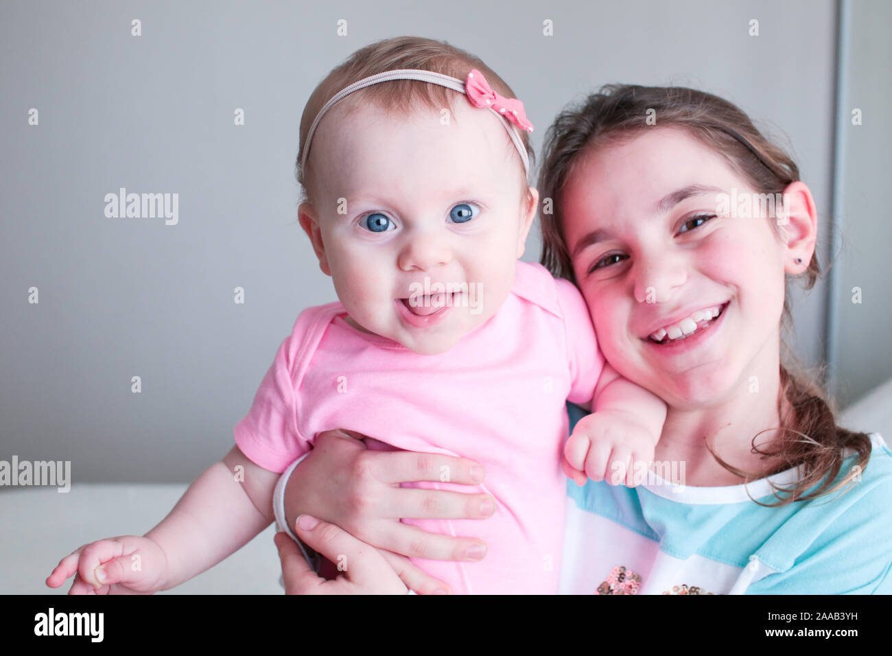 Close up Portrait of Two Sisters, Cute 8 Month Old baby Girl with Big blue Eyes and 8 Years Old School Age Girl With Brown Eyes , Happy Baby Girl Stock Photo