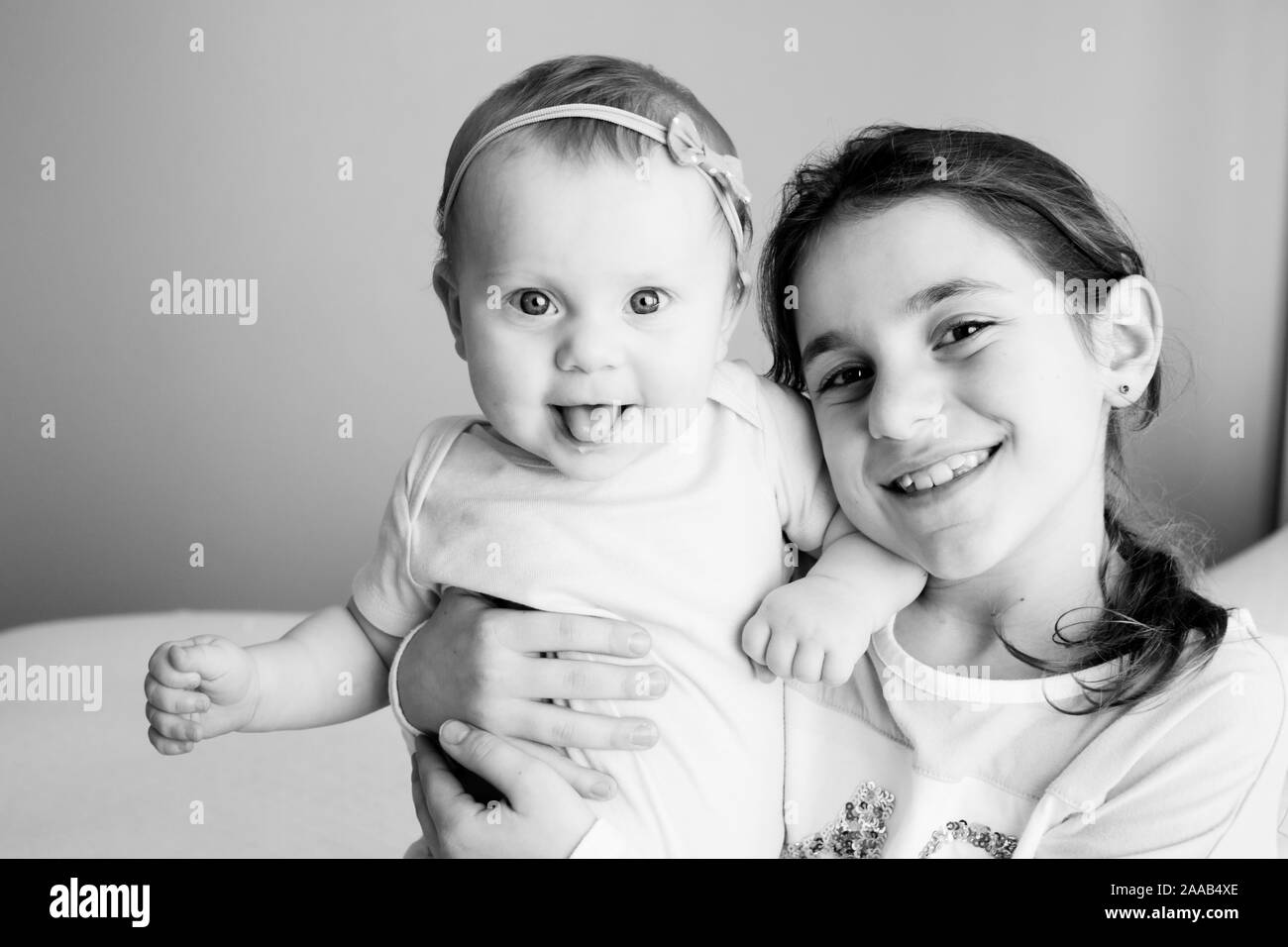 Close up Portrait of Two Sisters, Cute 8 Month Old baby Girl with Big blue Eyes and 8 Years Old School Age Girl With Brown Eyes , Happy Baby Girl Stock Photo