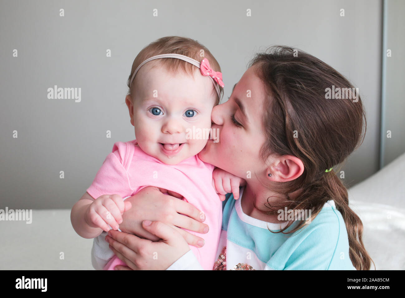 Close up Portrait of Two Sisters, Cute 8 Month Old baby Girl with Big blue Eyes and 8 Years Old School Age Girl With Brown Eyes , Happy Baby Girl Stock Photo