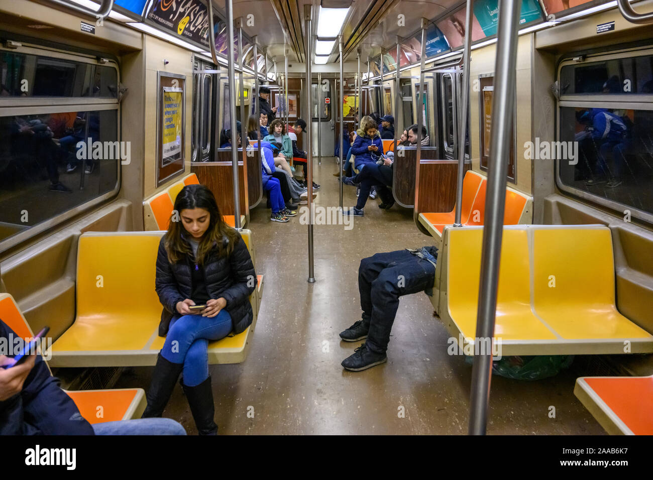 New York, USA, 9 November 2019.  Passengers use their mobile phones while ignoring an indigent man sleeping in the subway in New York City.   Credit: Stock Photo