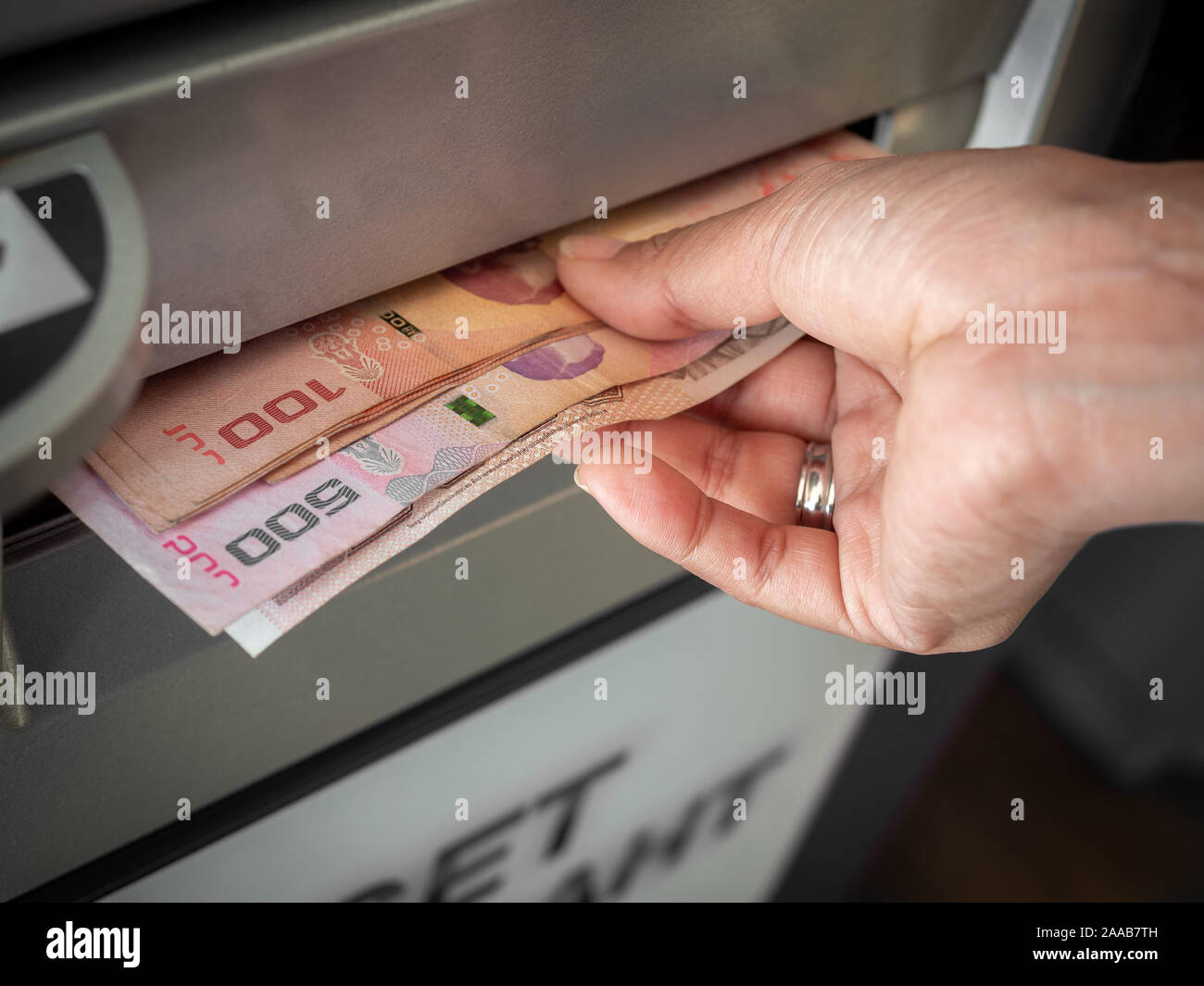 Close-up hand withdraw money, the banknotes thai baht from ATM machine in Thailand. Hand receiving cash money from ATM machine. Stock Photo