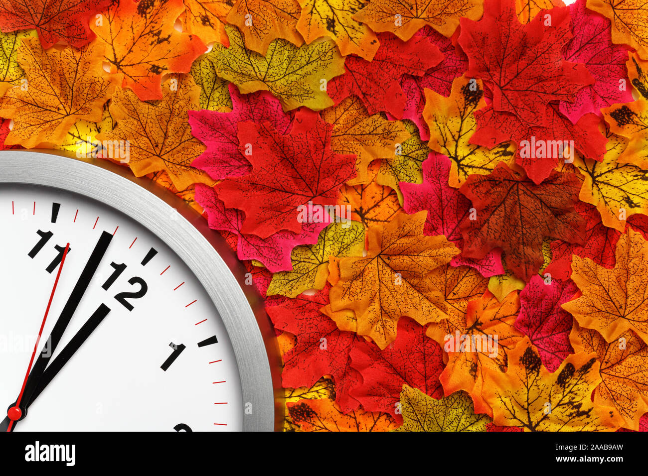 Clock on the colorful autumn maple leaves. Change of season time. Stock Photo