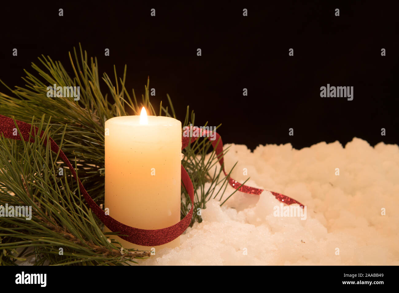 lit white candle and  pine needles in snow. Black Christmas Background with holiday theme. Stock Photo