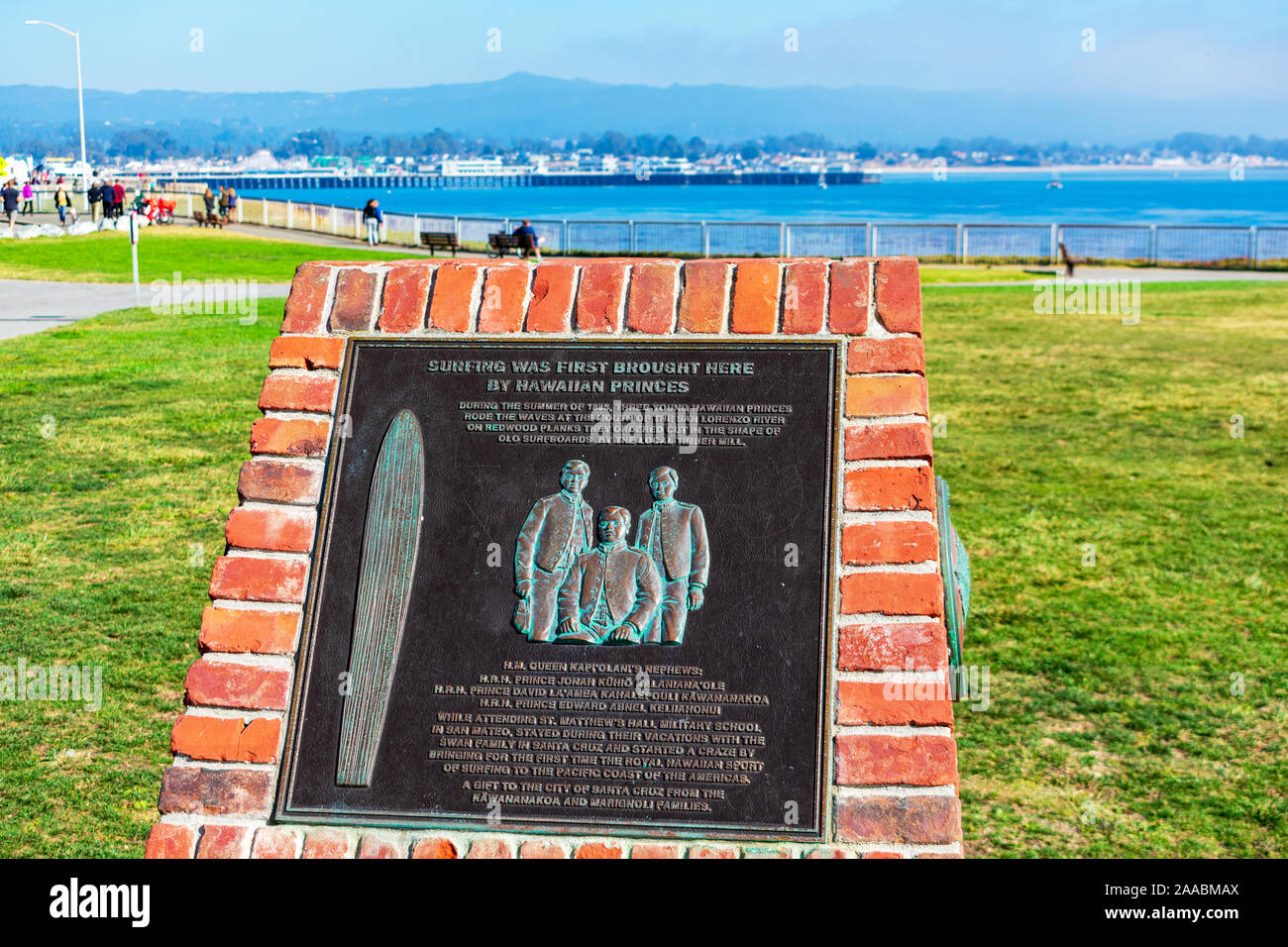 Memorial plaque honoring 1885 Hawaiian princes surfers at Santa Cruz Surfing Museum. Coastal view with residents, tourists, visitors enjoying Lighthouse Point Park - Santa Cruz, California, USA - 2019 Stock Photo