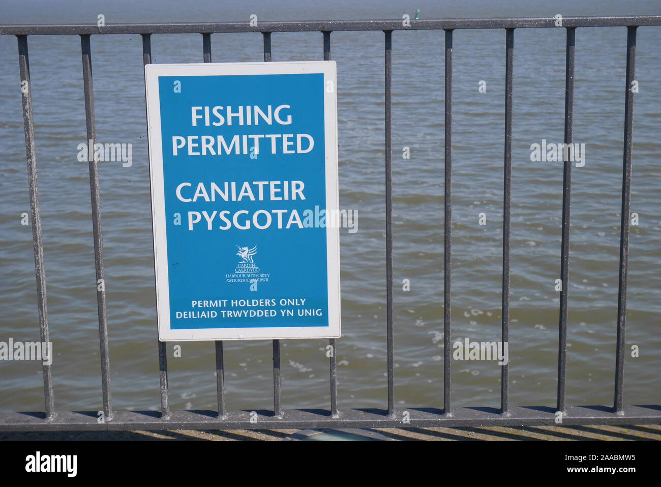 Bilingual sign on railings in English and Welsh saying Fishing Permitted and No Fishing, Cardiff Bay Barrage, Cardiff, Wales, United Kingdom Stock Photo