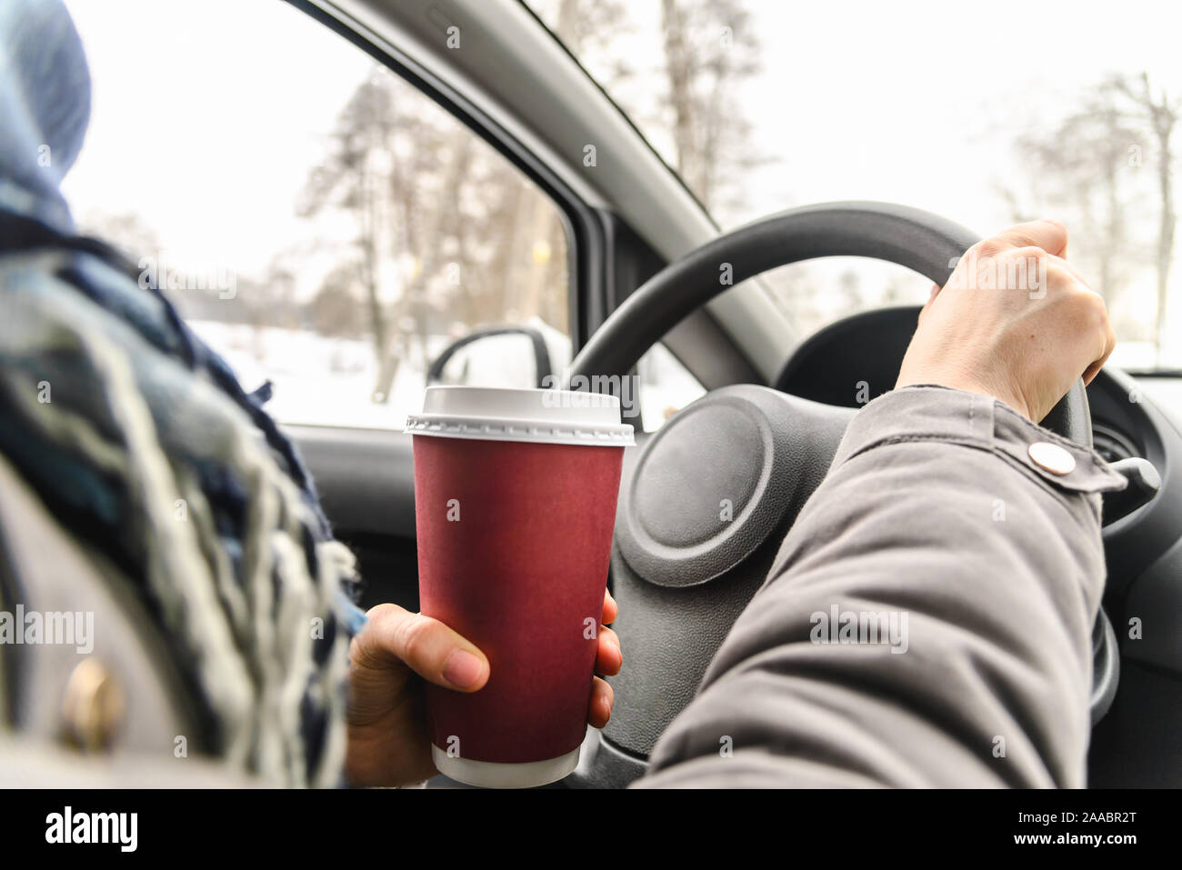 Driver drinking coffee in the car, driving and holding a steering wheel