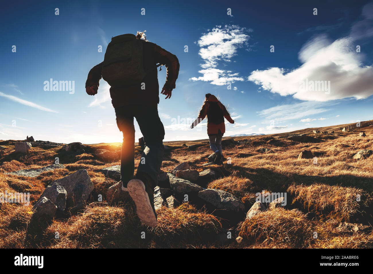 Couple of hikers run and jump against sunset mountains and sky Stock Photo