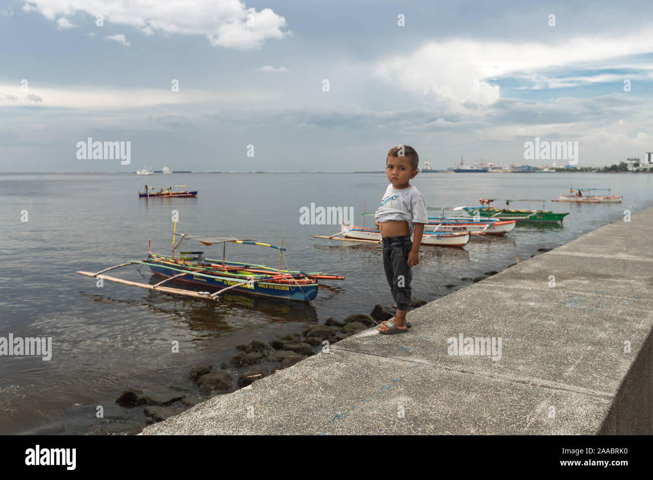 Manila, Philippines - July 7, 2017: Manila bay, boy look at the camera, sea and boats at background Stock Photo