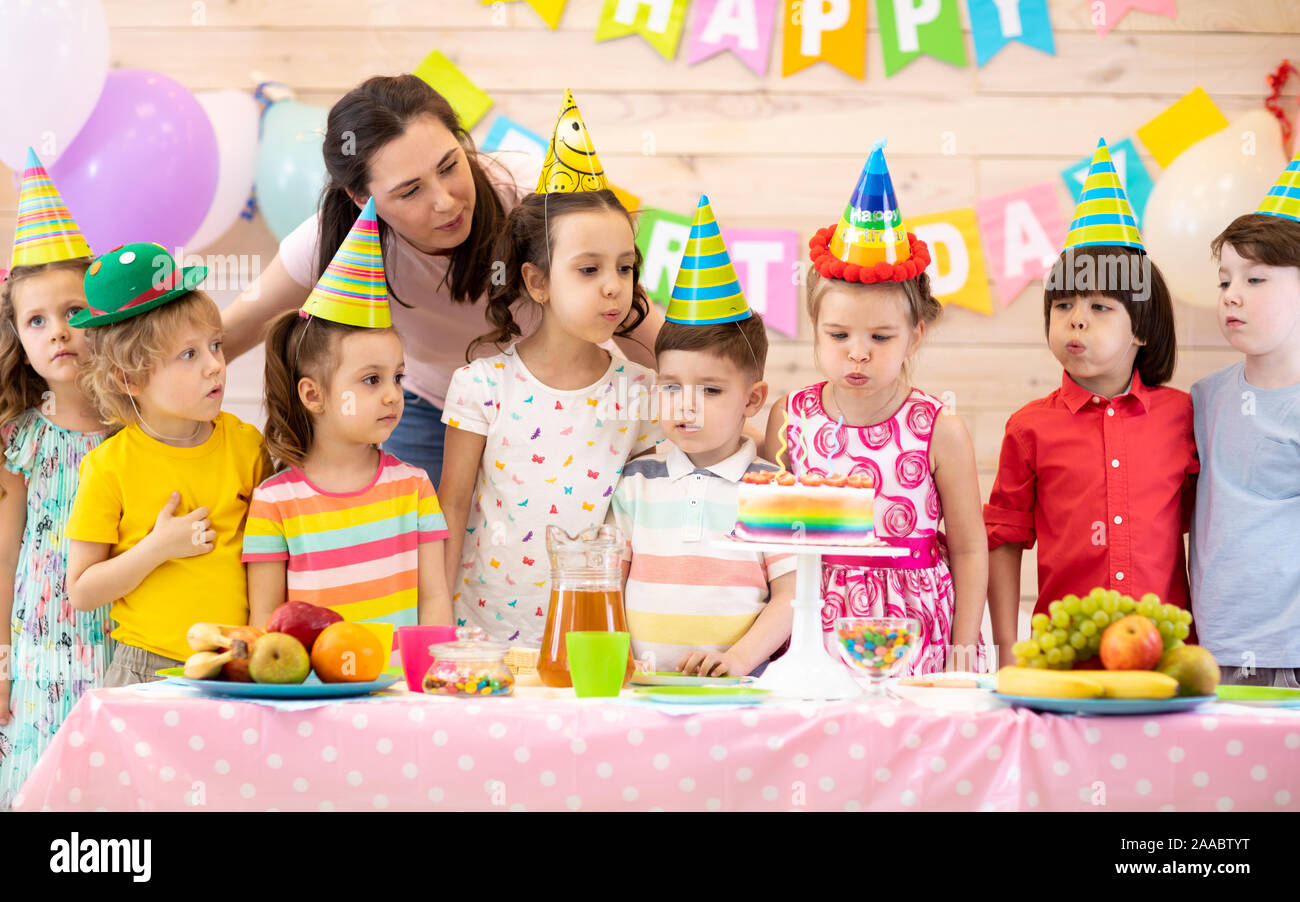 Group of adorable kids, birthday girl and her mom gathered around festive table. Birthday party for preschoolers Stock Photo