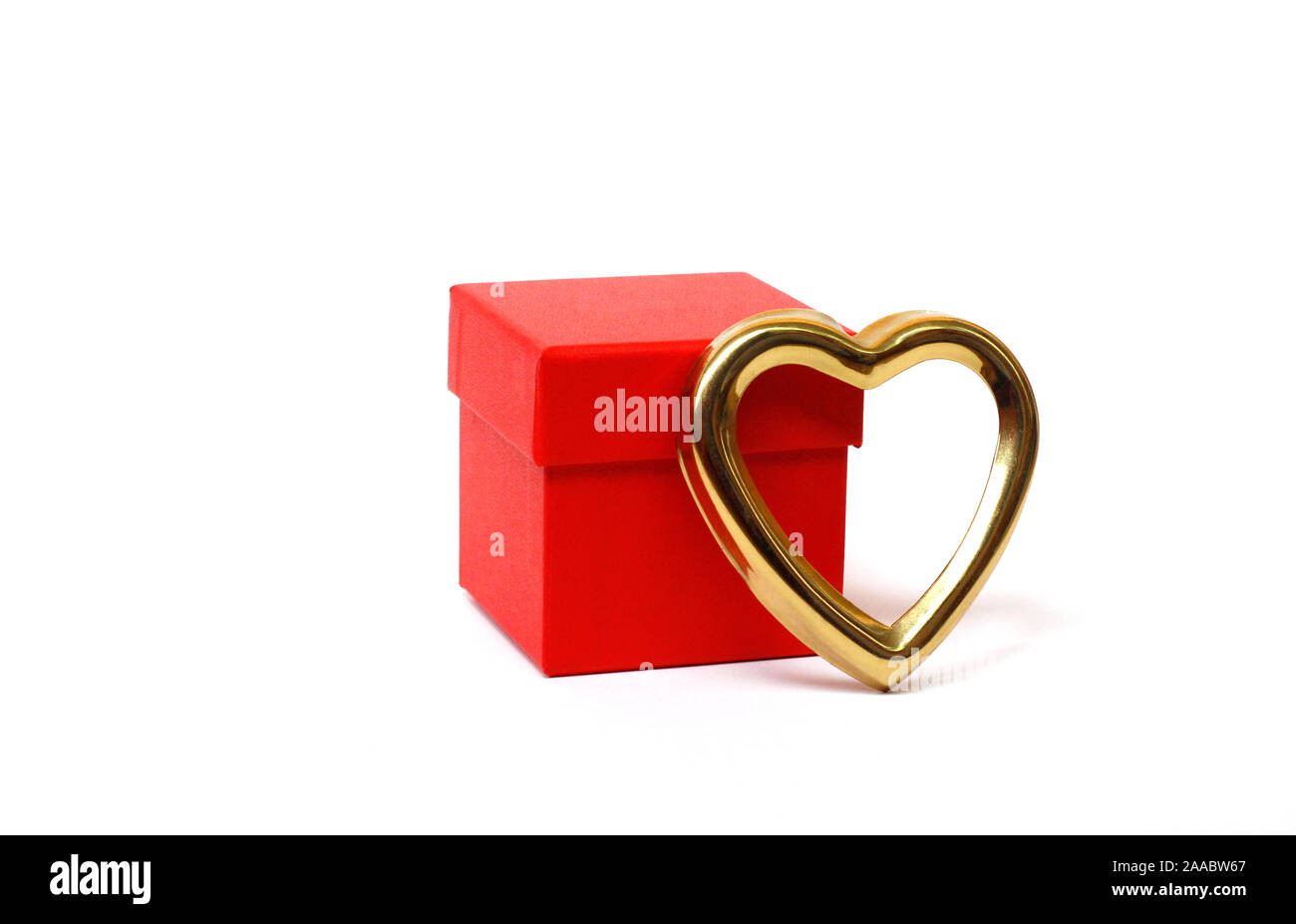 Red gift box with a closed lid on a white background. There is a place for text. Bright red box without inscriptions. Nearby is a golden heart. Gift f Stock Photo