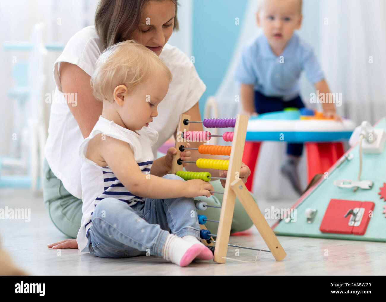 Kids playing on floor with developmental toys in kindergarten. Children have fun in nursery or daycare. Babies with teacher in creche Stock Photo
