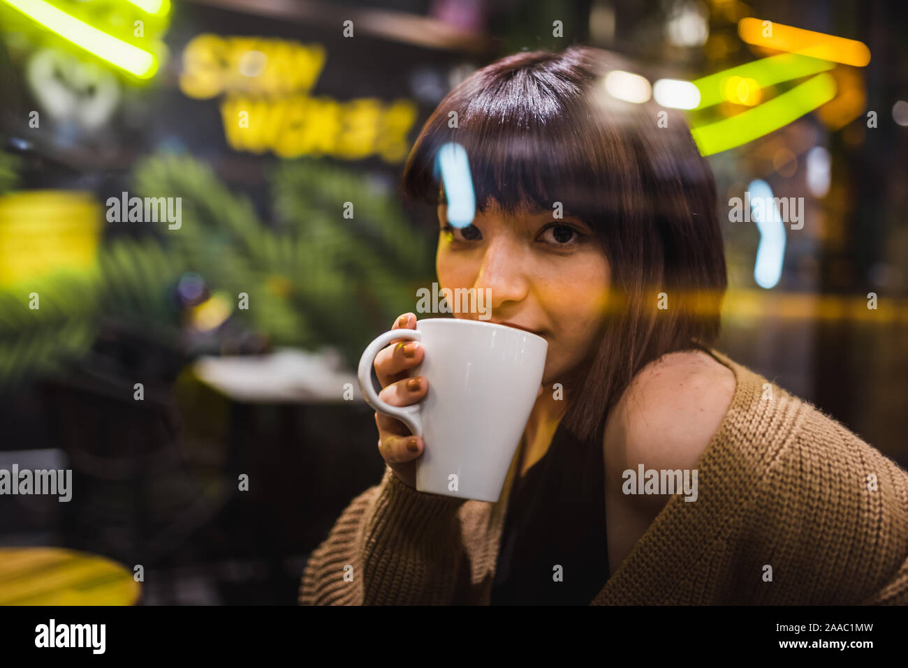 Beautiful young girl sits and drinks coffee at a trendy cafe or bar at