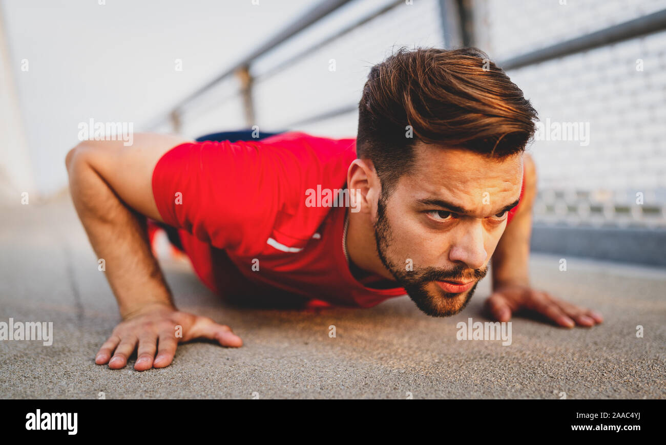 Beautiful male runner stretching before workout, fit man doing exercises outdoors Stock Photo