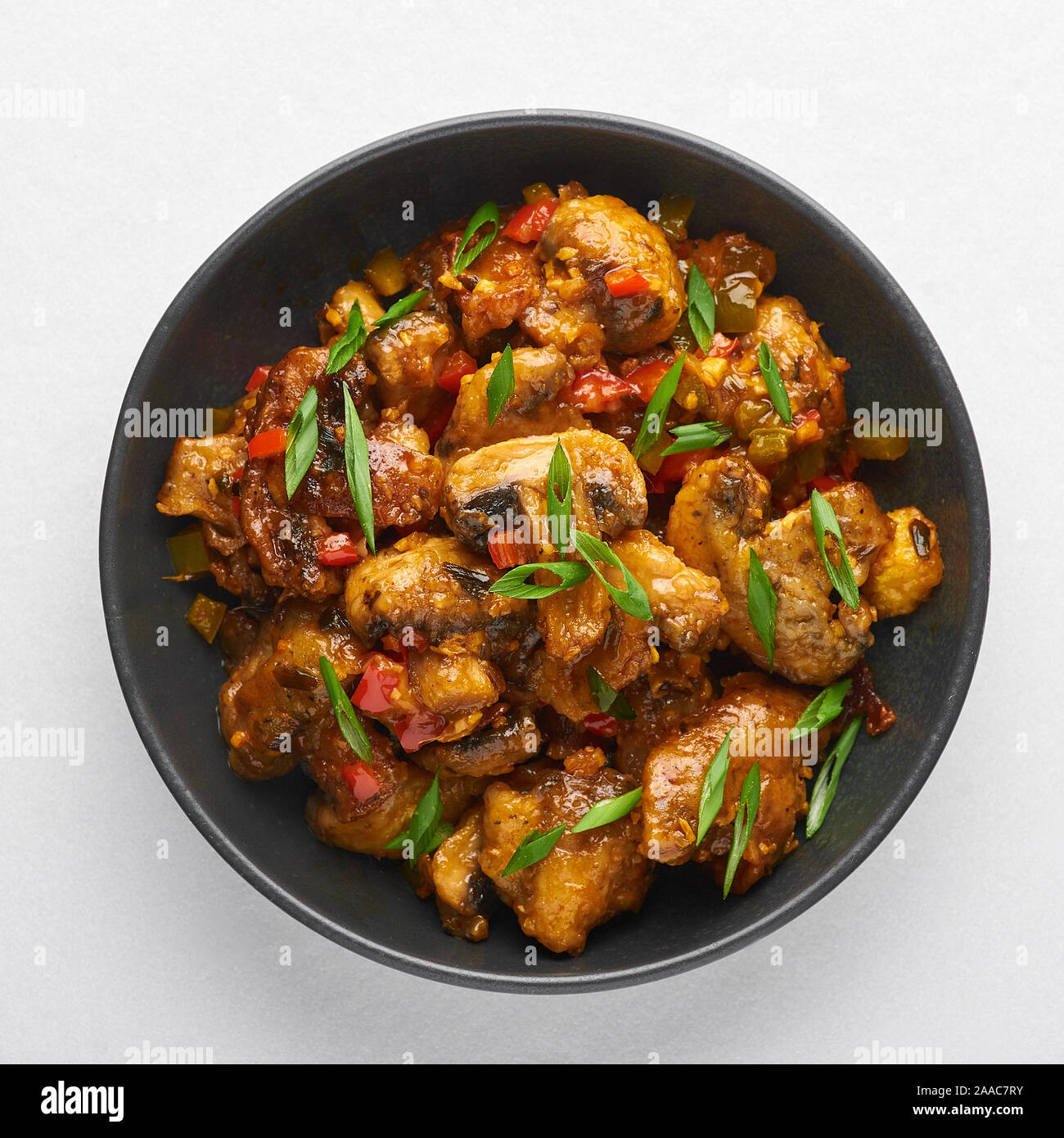 Mushrooms Manchurian dry in black bowl isolated at white background. Mushroom Manchurian - is indo chinese cuisine dish with deep fried mushrooms, bel Stock Photo