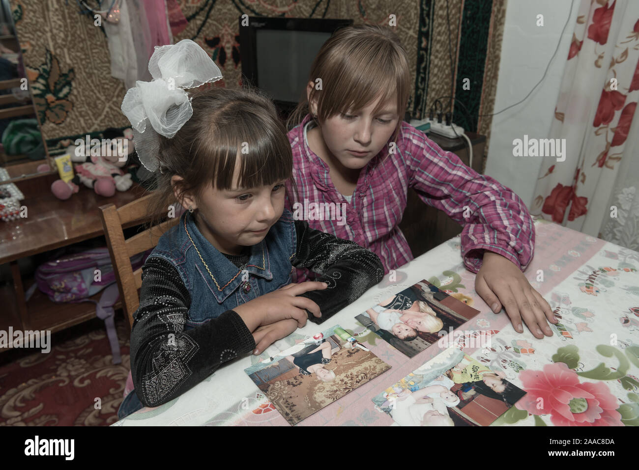 Sisters looking at photos of their mother who works in another country as a migrant worker.  The girls are looked after by their grandmother Stock Photo
