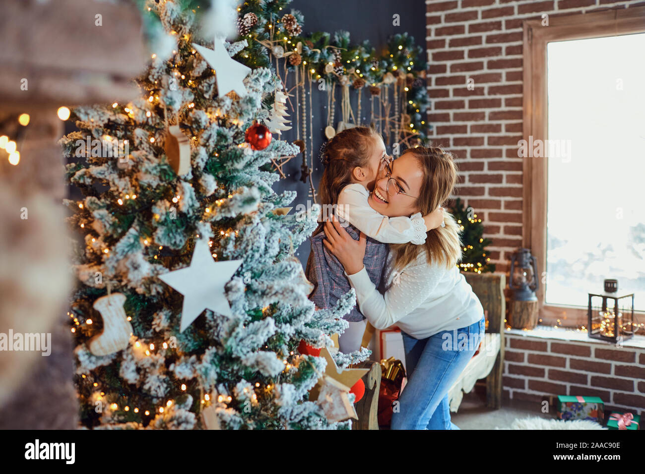 Mother and daughter hugging by the Christmas tree. Stock Photo