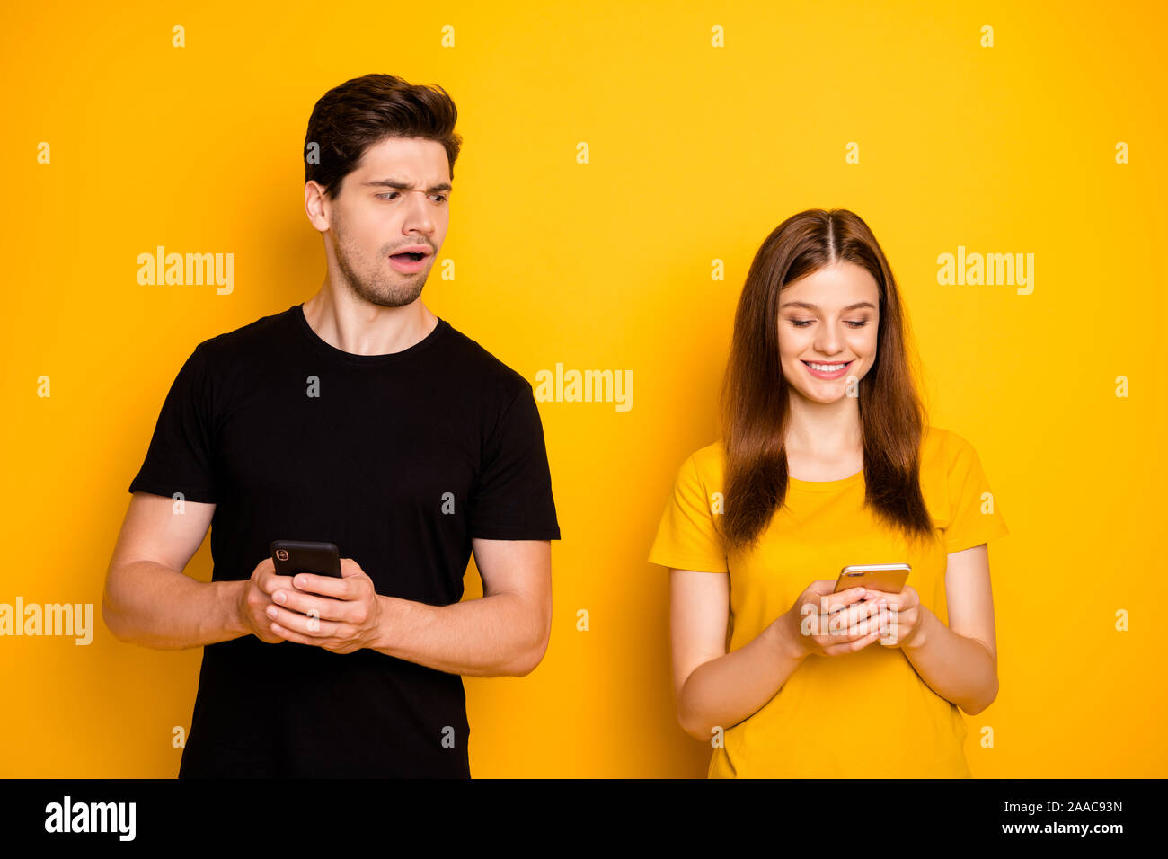 Photo of couple with boyfriend suspecting his girl of chatting to other guys and girlfriend not noticing her man watching her speak wearing black t Stock Photo