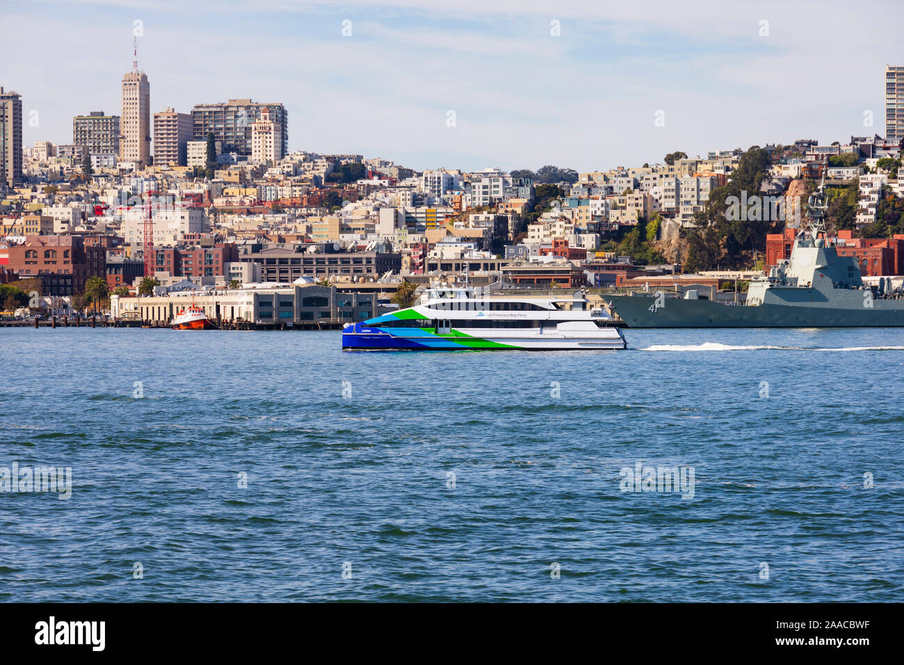 San Francisco Bay Ferry crossing in front of the San Francisco skyline, and HMAS Brisbane during Fleet Week 2019. California, United States of America Stock Photo