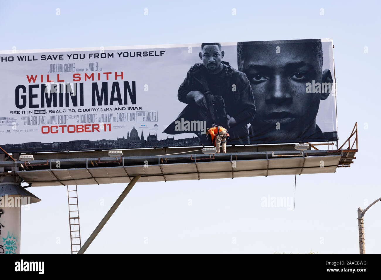 Huge billboard for the film Gemini, starring Will Smith, being erected by a man in orange hi viz jacket above the street. Los Angeles, California, USA Stock Photo